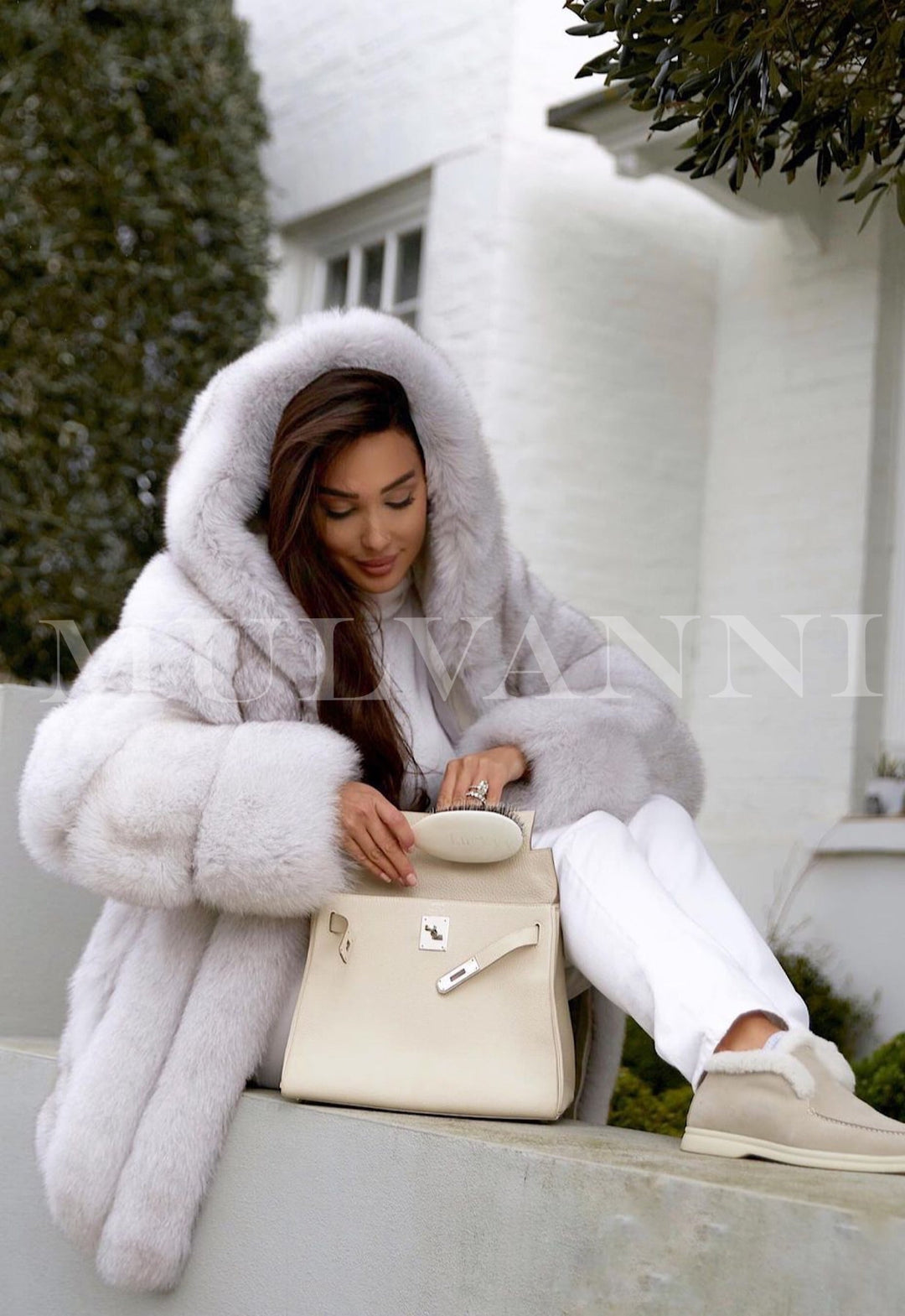 A woman wearing a luxurious white fox fur coat with a large hood, exuding elegance and warmth. The plush coat is perfect for winter, adding a sophisticated touch to her cold-weather attire.