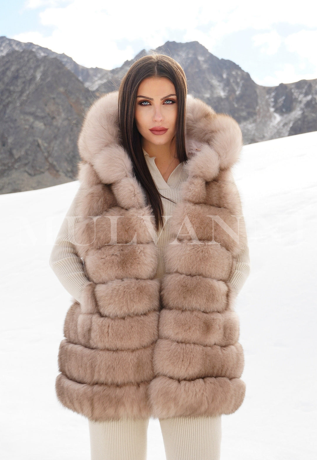 Model wearing a reversible merino wool parka and fox fur vest in snowy mountains, luxury designer coat for extreme and snow weather conditions.