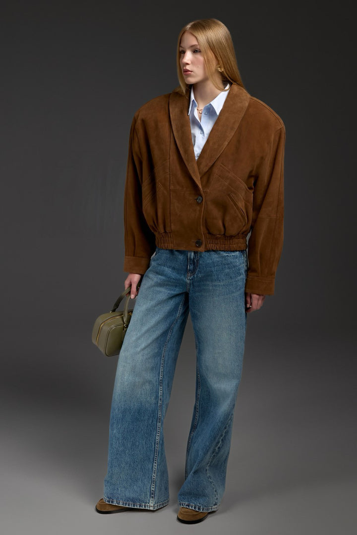 A woman is seen wearing a cropped brown suede jacket with wide, sculpted shoulders, making a sleek and sophisticated fashion statement.