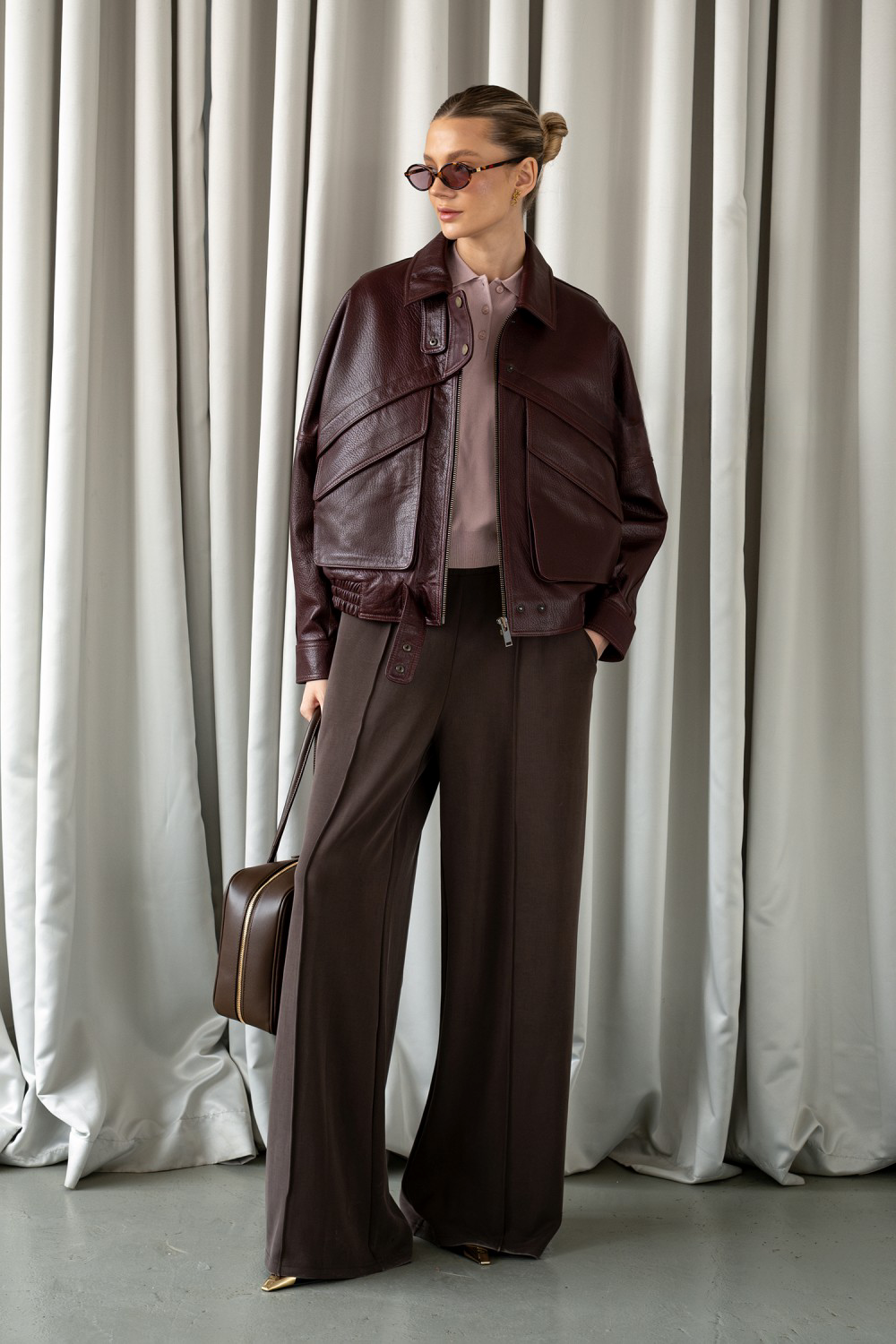 Model wearing dark burgundy leather jacket with gold hardware, exuding modern elegance and fashion-forward style.