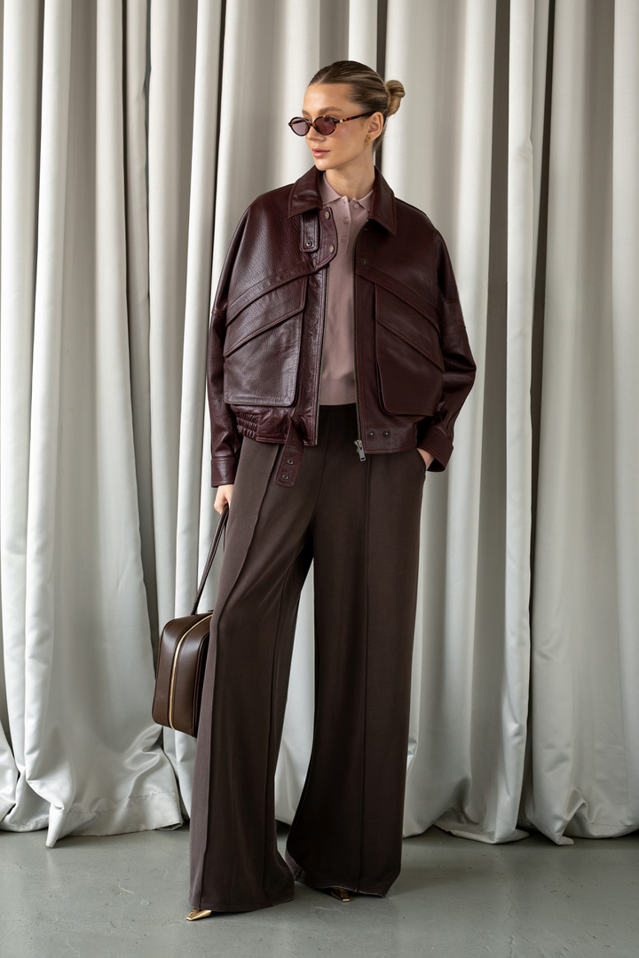 Model wearing dark burgundy leather jacket with gold hardware, exuding modern elegance and fashion-forward style.