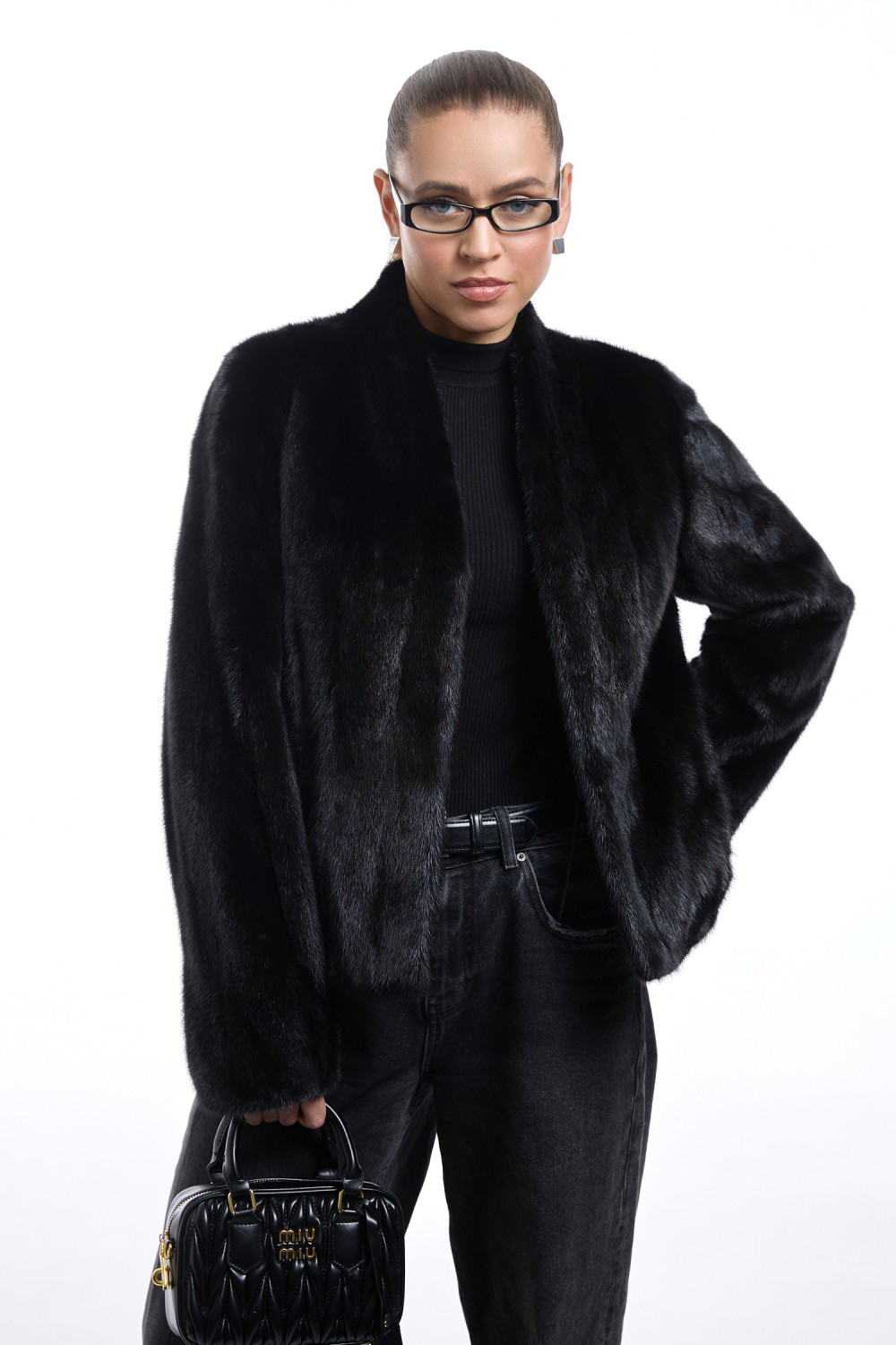 Model wearing a short black mink fur coat, styled with dark jeans and a handbag, showcasing elegant winter fashion.