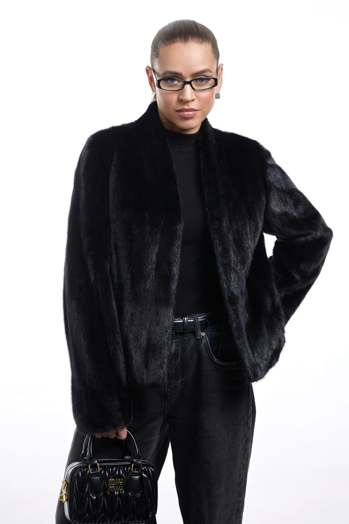 Model wearing a short black mink fur coat, styled with dark jeans and a handbag, showcasing elegant winter fashion.