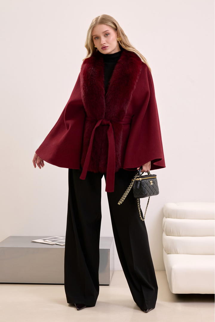 Elegant woman in burgundy cashmere cape with fox fur trim, showcasing rich color and luxurious winter style.