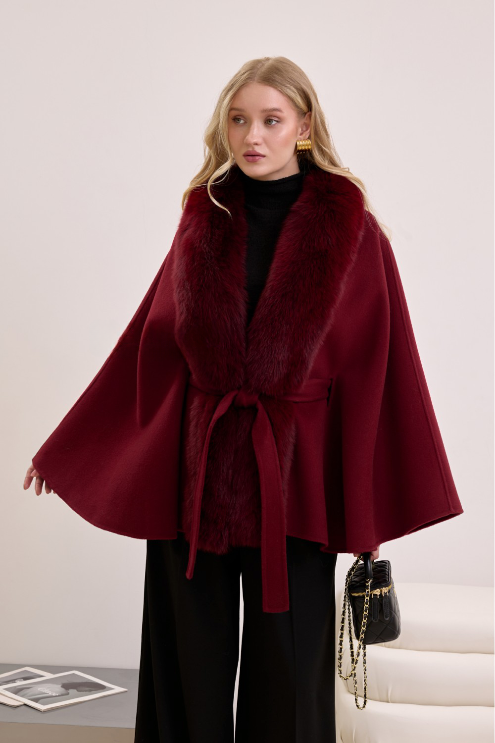 Deep burgundy cashmere cape with plush fox fur details, worn by woman for an elevated cold-weather look.
