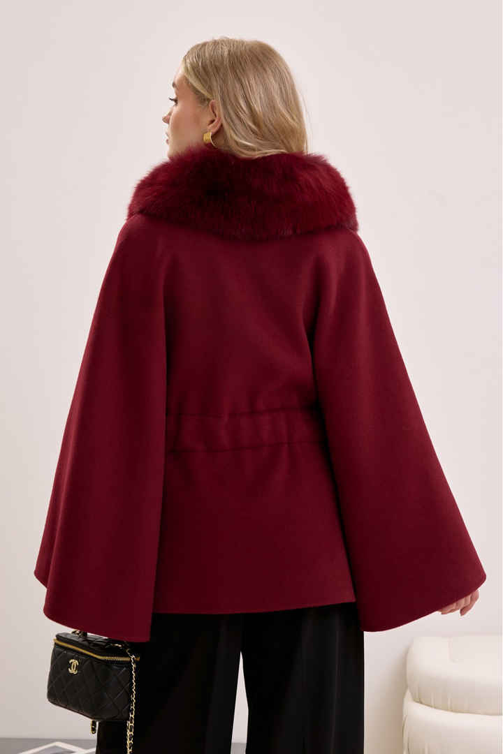 Woman wearing burgundy fox fur-trimmed cape, combining bold color with classic winter luxury.
