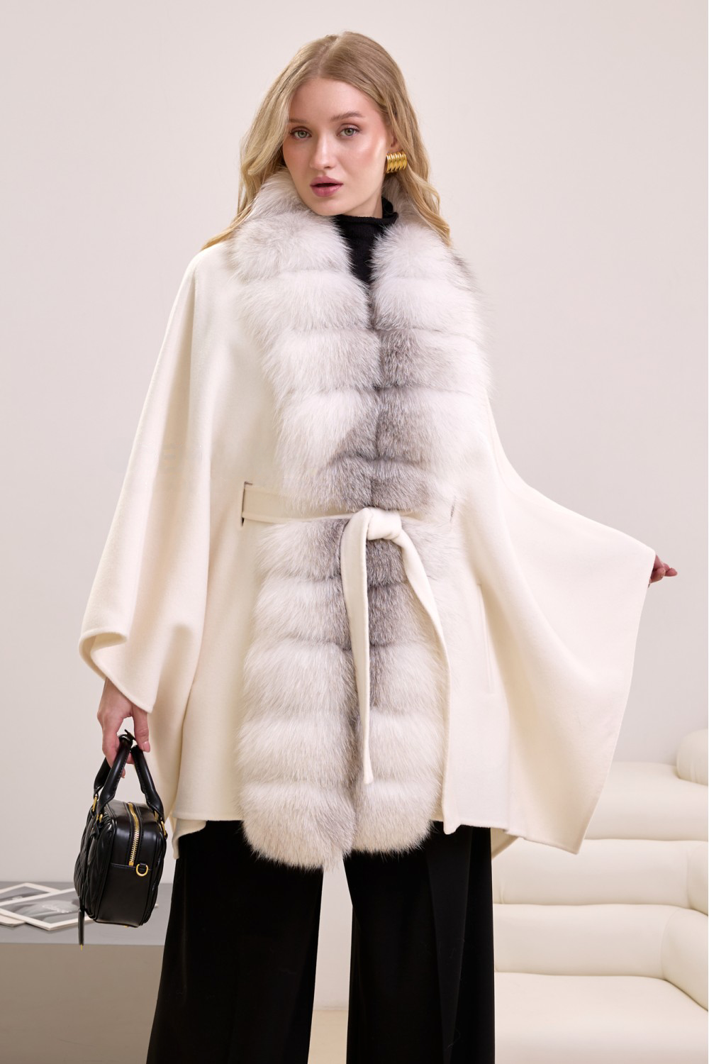 Elegant woman in off-white cashmere cape with fox fur trim, showcasing timeless winter luxury.