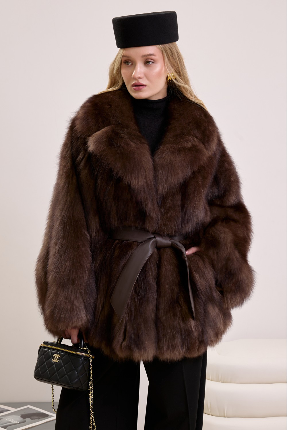 Elegant woman wearing a natural fox fur coat cinched at the waist with a leather belt for a refined, feminine silhouette.
