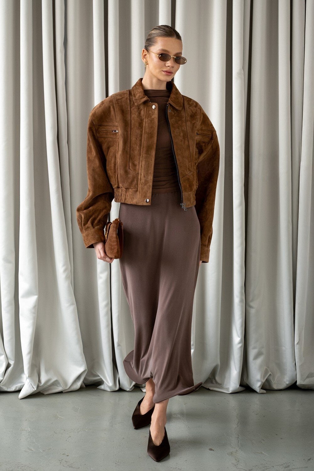 A woman wearing a rich whiskey suede cropped bomber jacket, featuring ultra-soft genuine suede and a refined silhouette that sits just above the waist for a modern, elegant look.