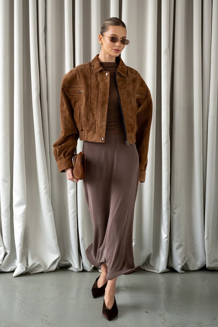 A woman wearing a rich whiskey suede cropped bomber jacket, featuring ultra-soft genuine suede and a refined silhouette that sits just above the waist for a modern, elegant look.