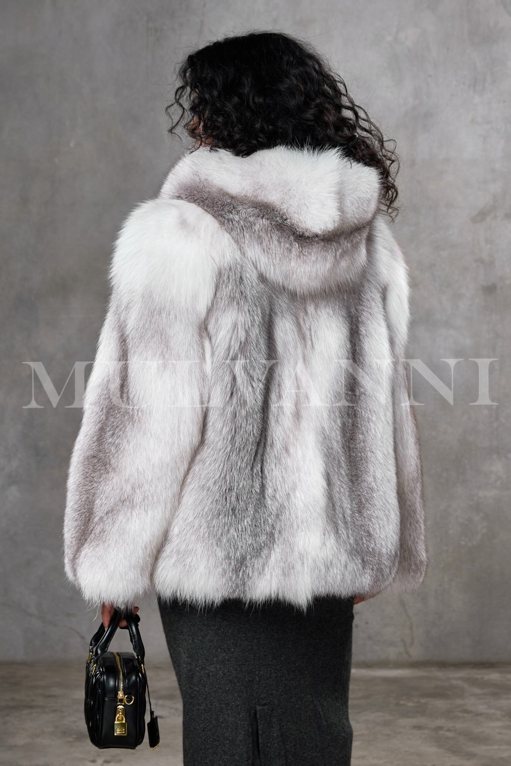 This Arctic fox fur coat, worn by a woman, showcases unmatched softness and a loose, elegant fit with a cozy hood, providing exceptional warmth suitable for temperatures as low as -25ºC.
