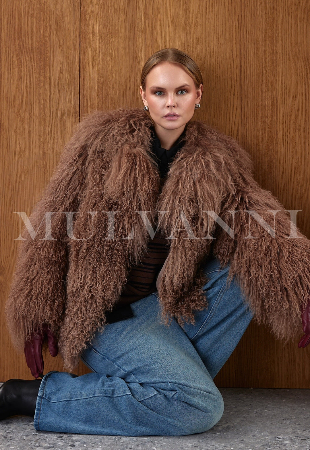 A woman wears a luxurious brown Mongolian fur coat with long sleeves and a voluminous silhouette, exuding warmth and high-fashion elegance.