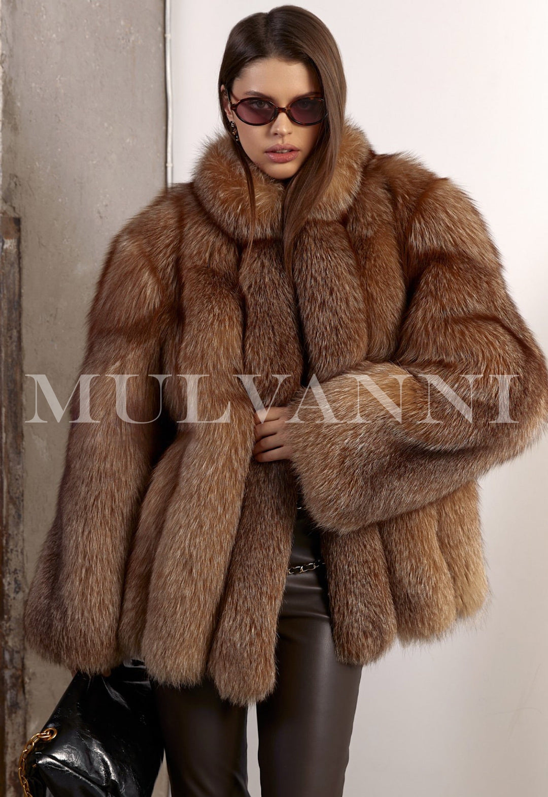 Woman wears a luxurious oversized fox fur coat styled with brown leggings and a sleek black leather handbag, exuding effortless winter elegance.