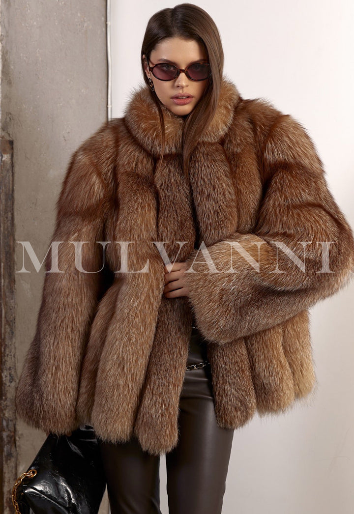 Woman wears a luxurious oversized fox fur coat styled with brown leggings and a sleek black leather handbag, exuding effortless winter elegance.