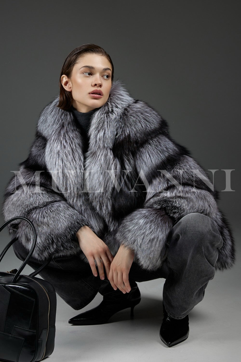Styled in a luxurious silver-toned fox fur coat, the woman adds a modern edge with a structured black leather bag, blending elegance with urban chic.