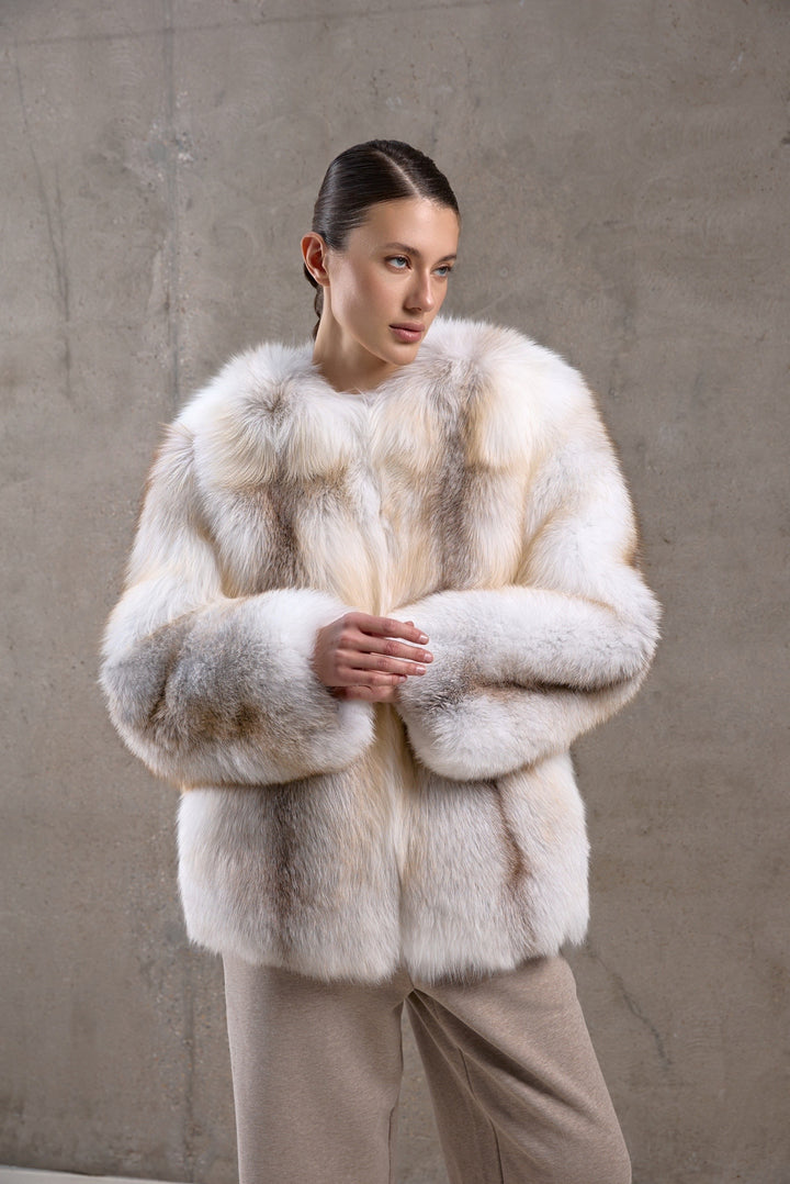 A woman exudes sophistication in a full-bodied fox fur coat featuring golden cross tones, designed for elegance and resilience against harsh climates.