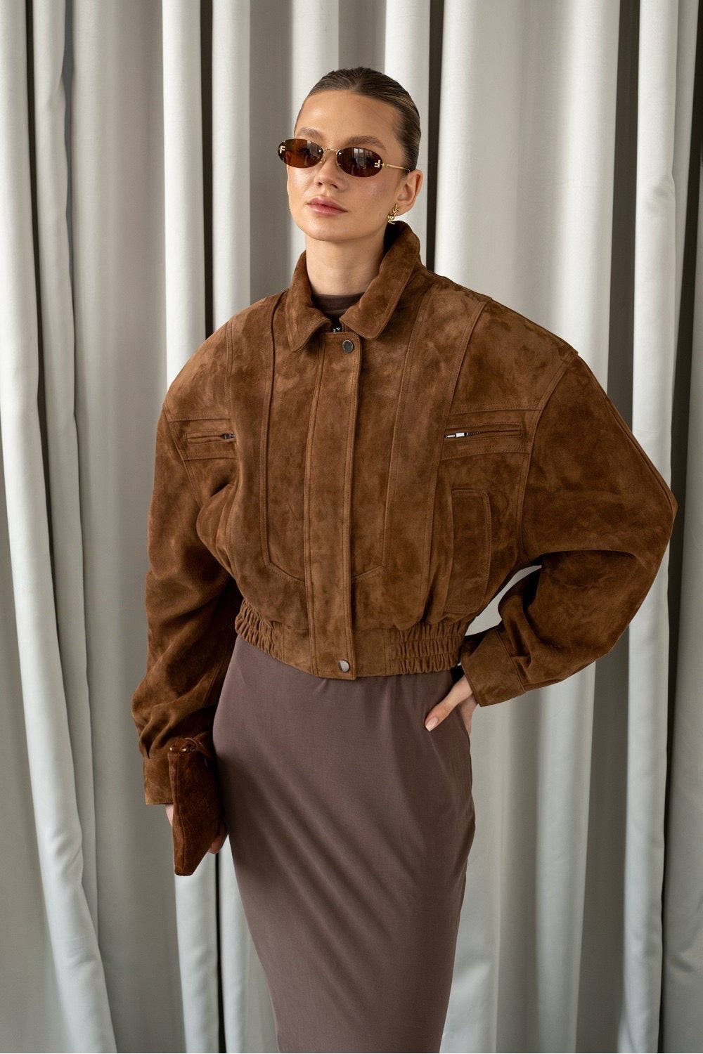 A woman models a whiskey-colored suede bomber jacket with a refined cropped fit, showcasing its soft texture and chic, sophisticated design.