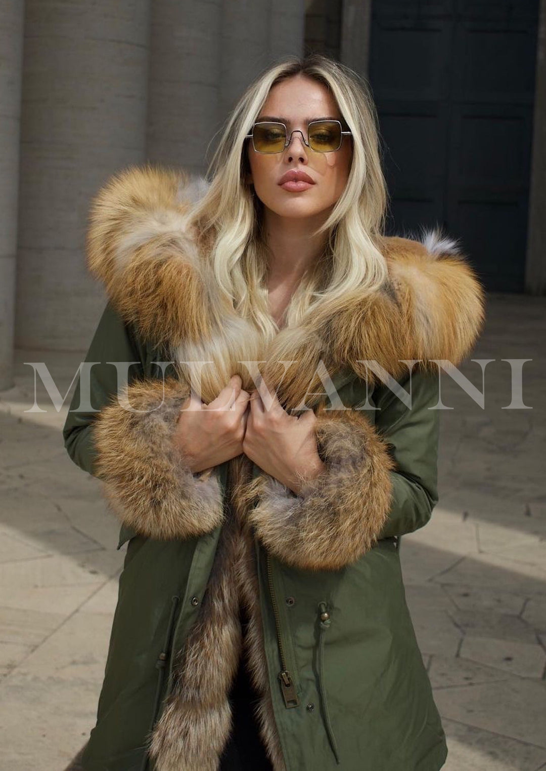 A woman dressed in a green parka with a striking red fox fur lining. The fur accents provide a touch of luxury, making the coat both functional and fashionable for winter outings.