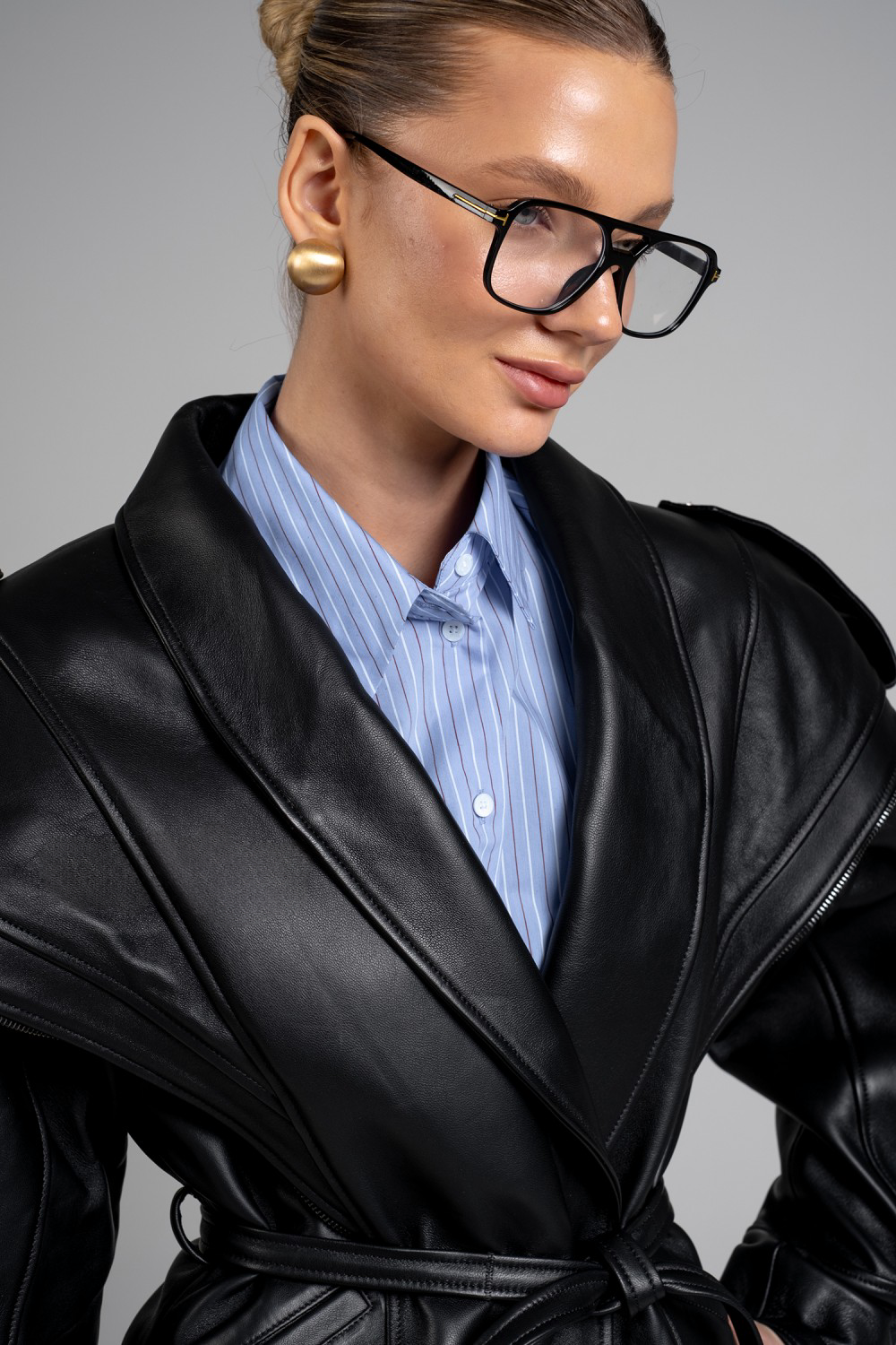 A woman dressed in a Jacket, a striking black leather piece with bold shoulders, asymmetric front zip, and a cinched waist for a sharp, contemporary silhouette.