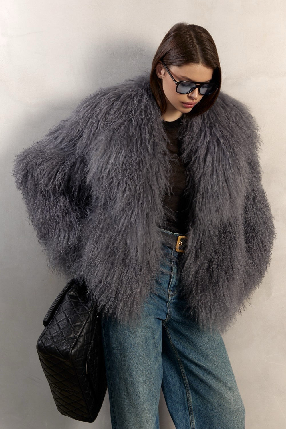 A woman wearing a luxurious grey Mongolian fur coat, beautifully handcrafted from thick, genuine Mongolian fur with a dramatic collar, long sleeves, and elegant one-piece design.