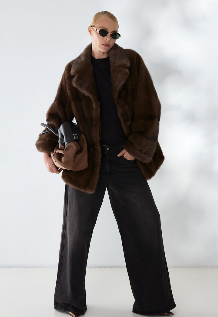 A woman wears a dark brown mink fur coat with a modern yet classic design, showcasing velvety softness and sophisticated style with effortless grace.