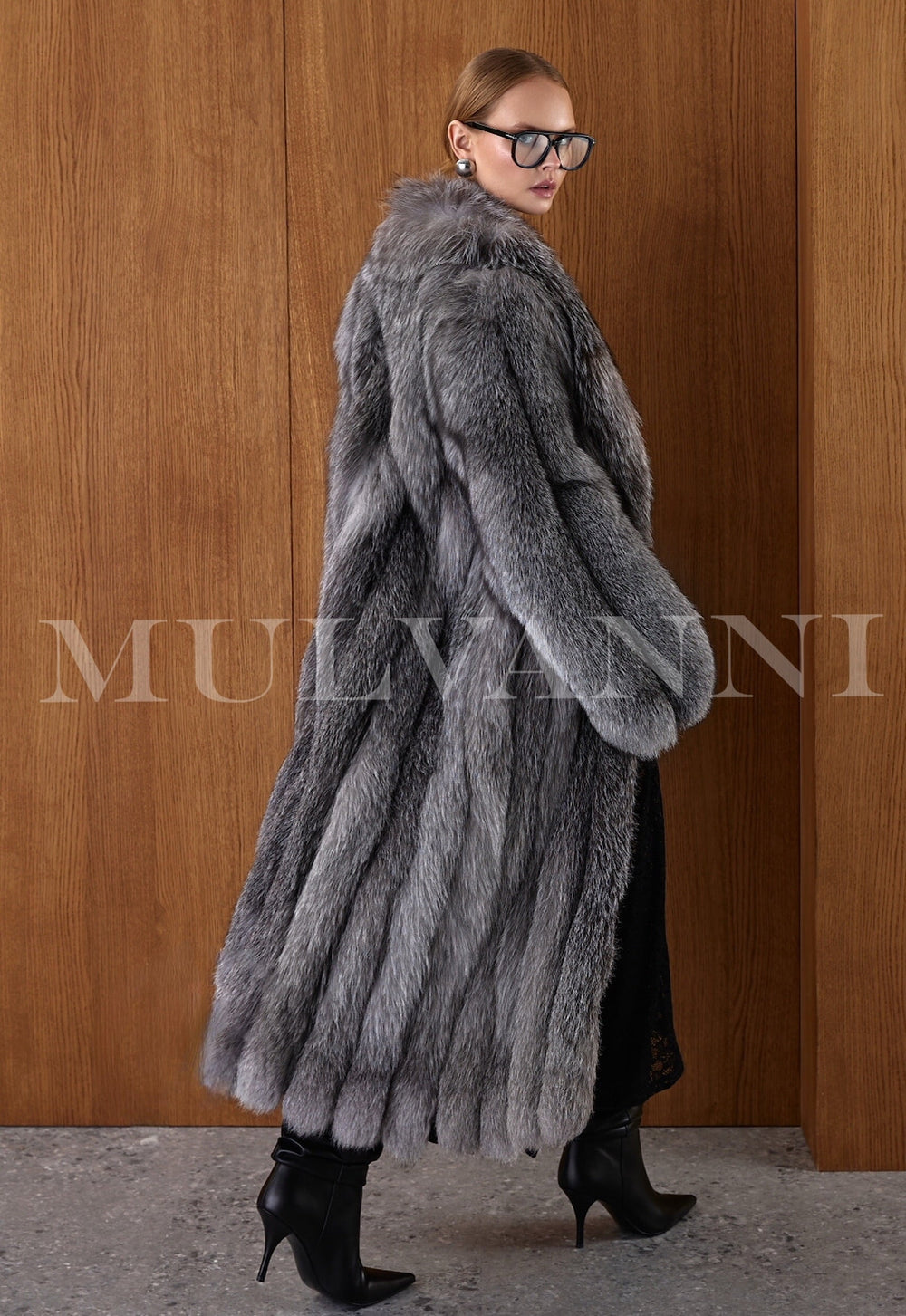 Side view of a woman in a 130 cm natural fox fur coat, showcasing the sleek elongated silhouette and rich texture of the Silver Frost Fox.