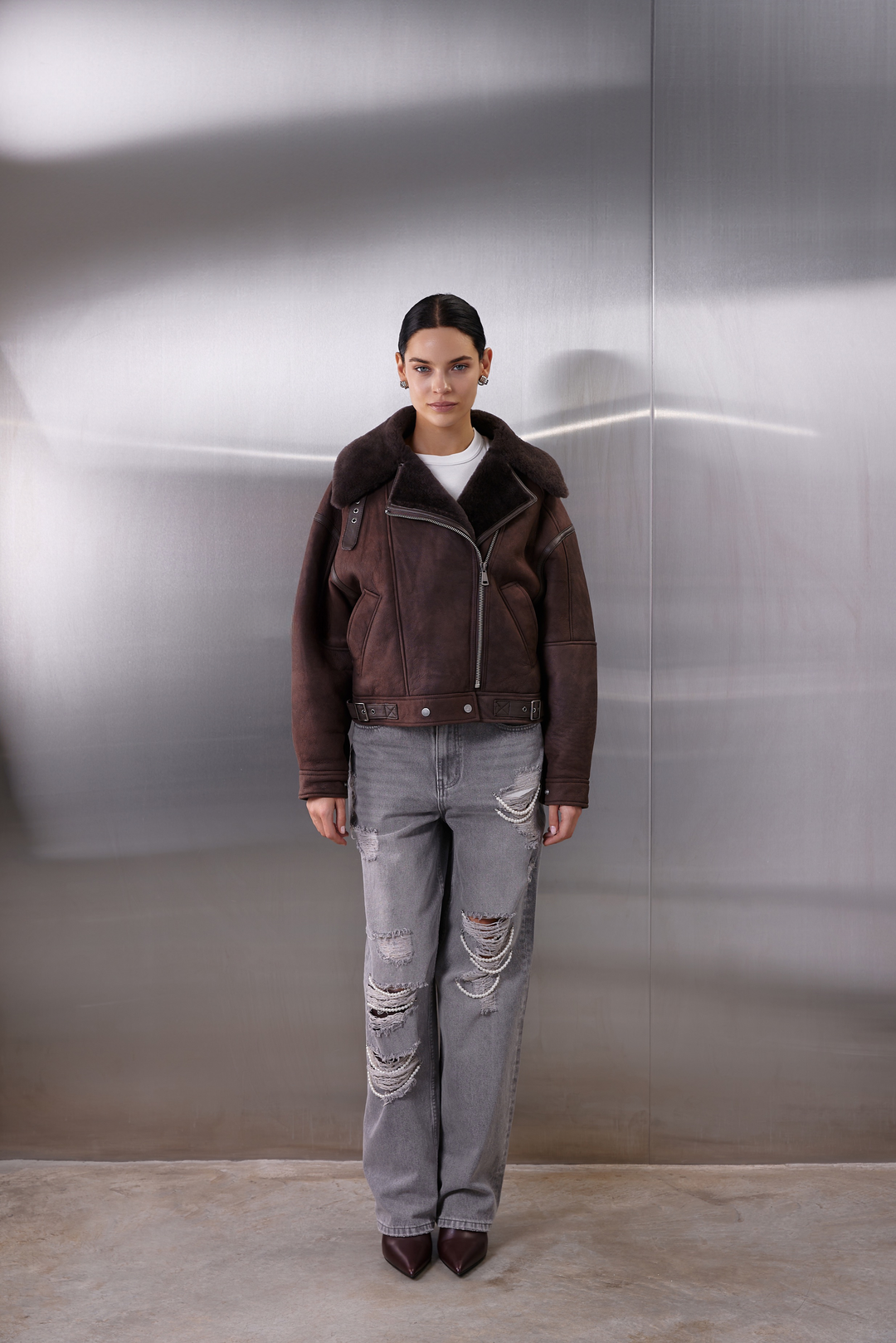 A woman wearing a warm and cozy brown shearling aviator bomber, handcrafted from thick sheepskin and reimagined with a cropped, oversized style ideal for cold-weather insulation.