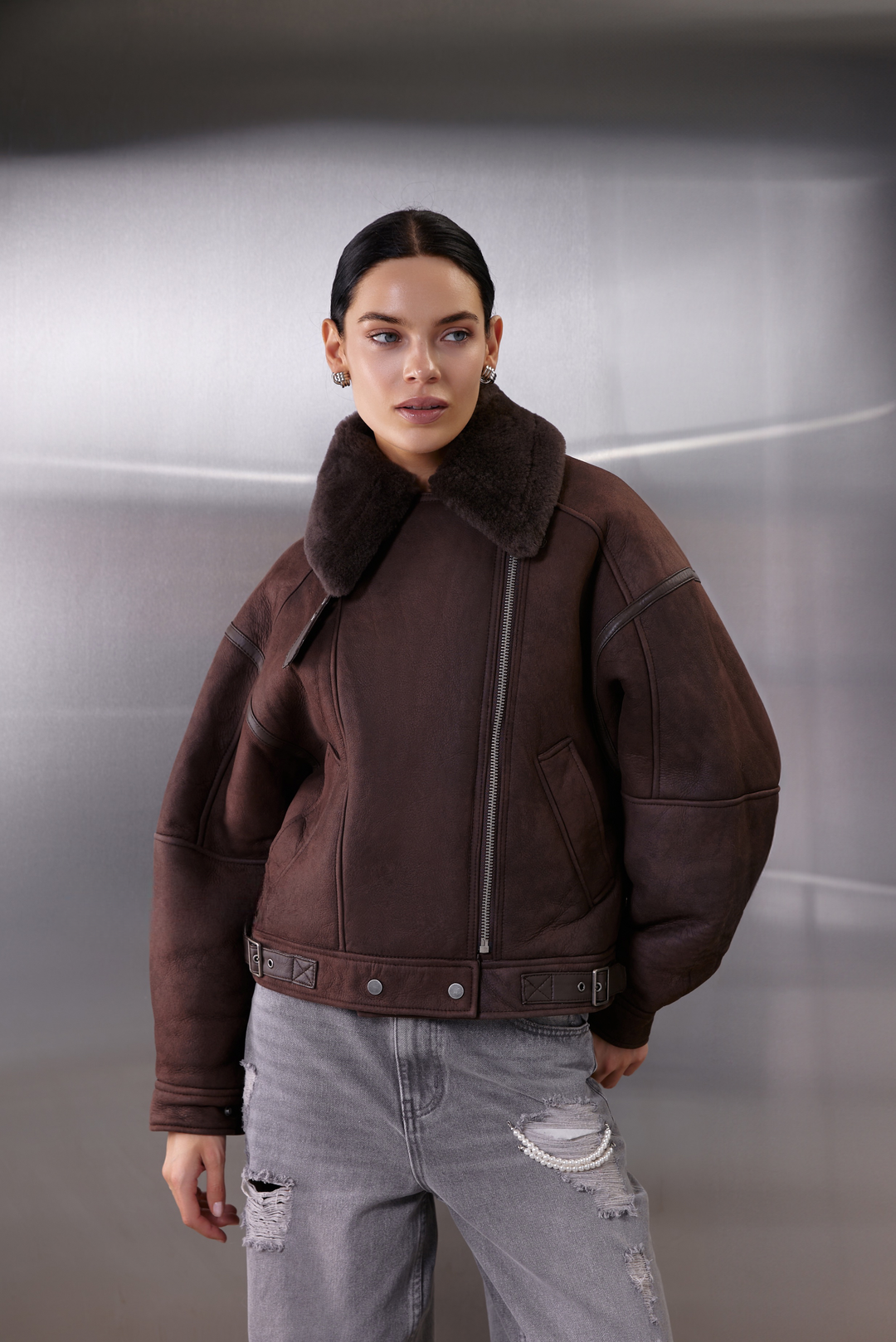 A woman models a thick brown sheepskin aviator bomber with shearling lining, designed in a cropped, oversized silhouette for both warmth and stylish winter layering.