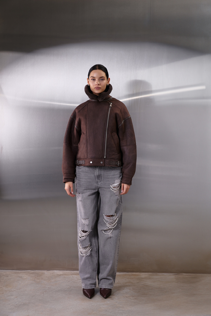 A woman dressed in a heavyweight brown leather aviator jacket with soft shearling lining, combining a voluminous, sporty fit with a feminine cropped cut—perfect for layering over sweaters.