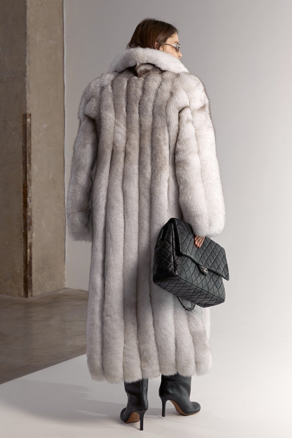 A woman dressed in a striking natural white fox fur coat with mixed grey tones, offering a soft, dense texture and a flattering, floor-length fit built for temperatures as low as -25ºC.