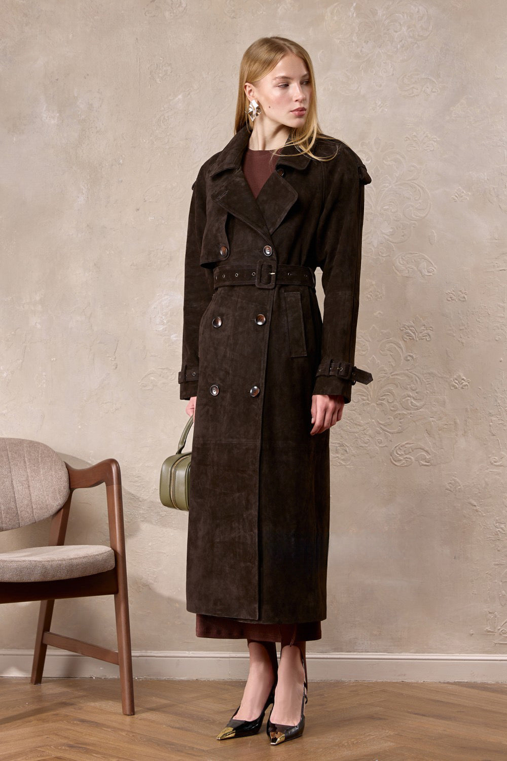 A woman wears the Hatti suede leather trench coat, featuring a tailored double-breasted design that flatters her figure with modern sophistication.
