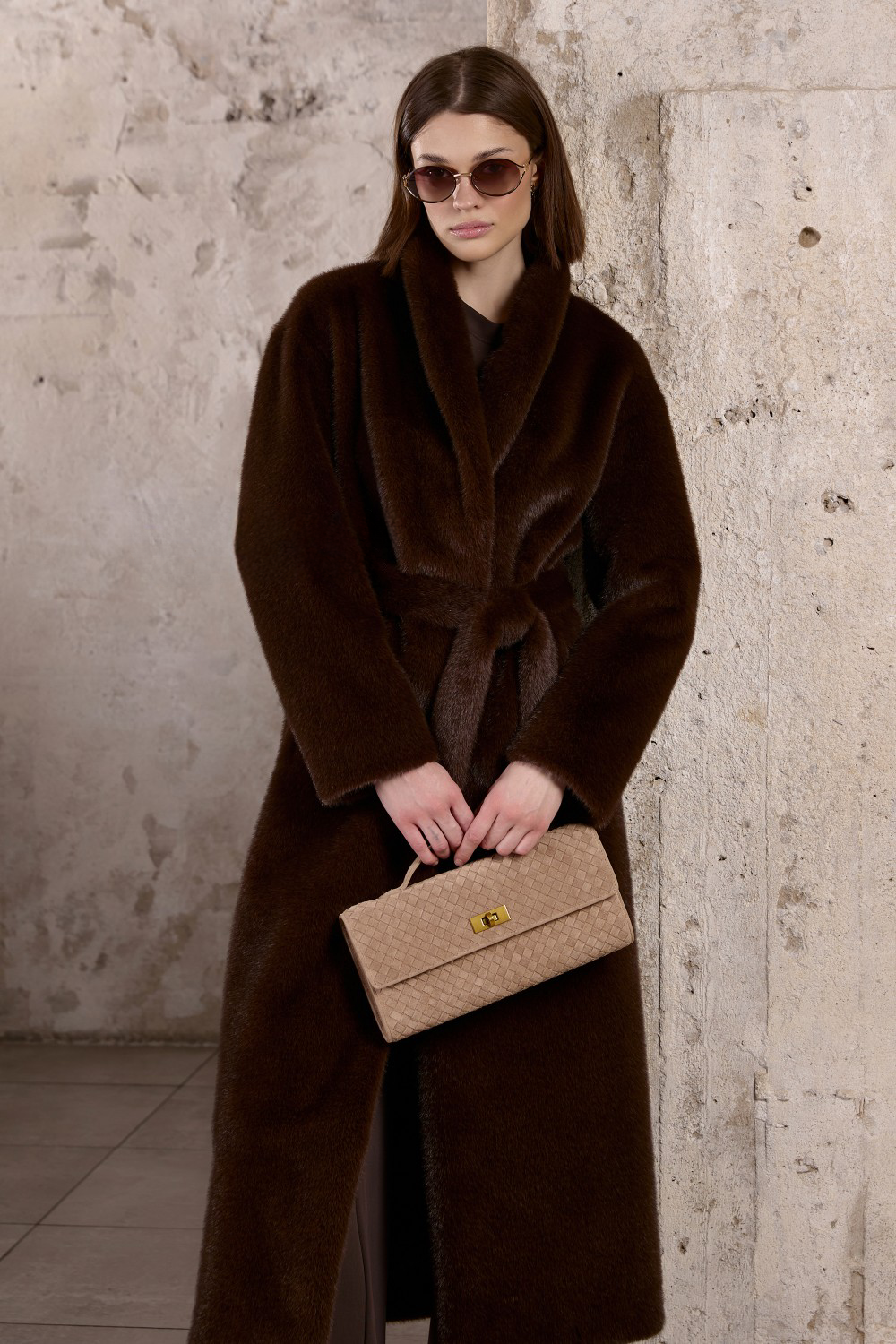 A woman models this statement longline coat with spacious oversized pockets and prominent collar and lapels, enhanced by the matching thick faux fur belt worn to accentuate the waist with stylish flair.