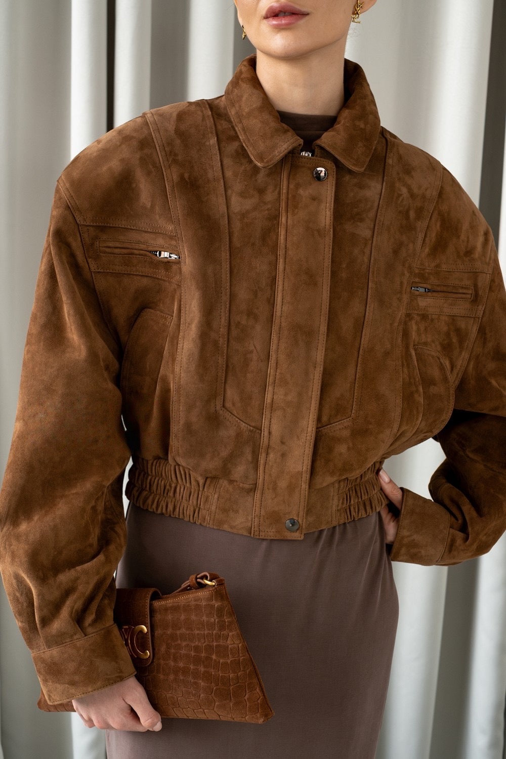 A woman dressed in a genuine suede cropped bomber jacket in a warm whiskey tone, combining standout style, modern structure, and elegant layering versatility.