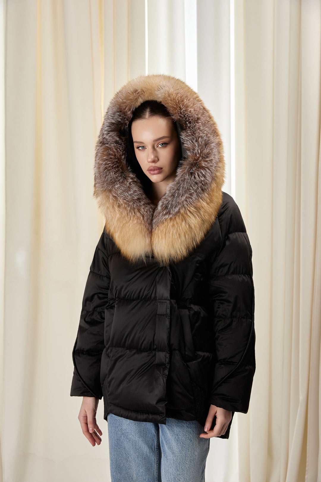 A woman dressed in a sleek black down jacket featuring a luxurious fox fur hood, perfect for cold weather with a fashionable edge.