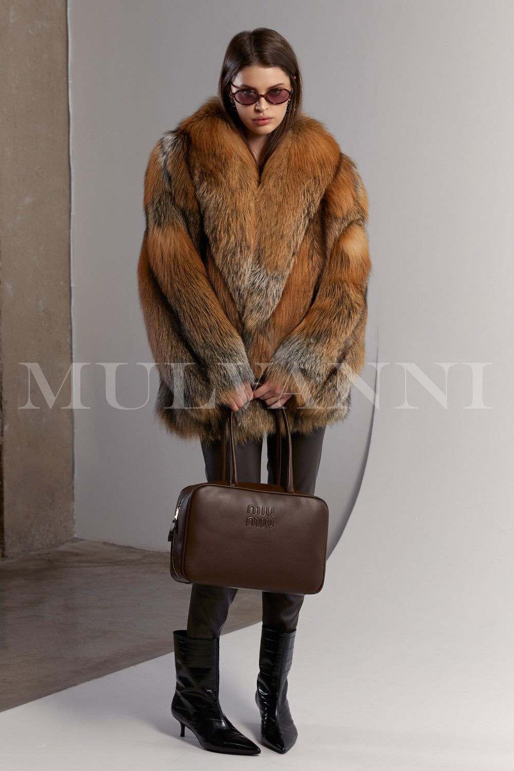 Styled in natural red fox fur, the woman pairs the plush coat with sleek brown leggings and a brown leather bag, creating a rich, sophisticated ensemble.