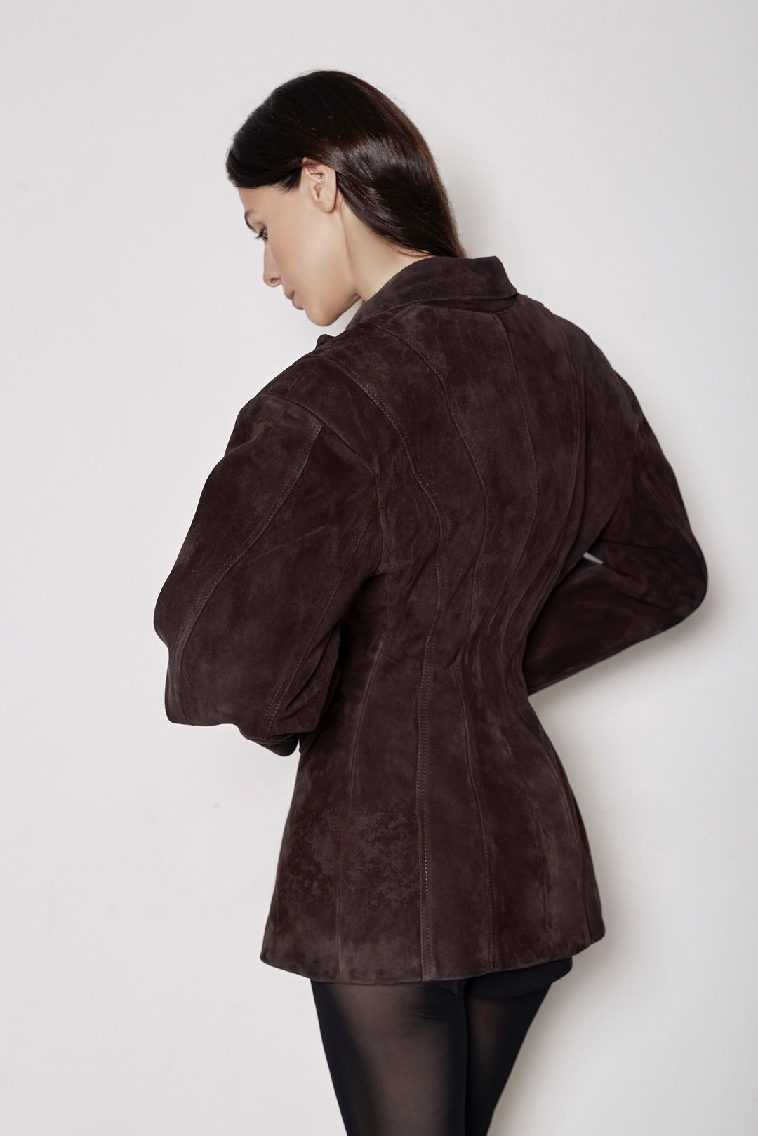 A woman seen from the back wearing a brown suede blazer paired with black tights, showcasing the blazer’s tailored fit and elegant design from every angle.