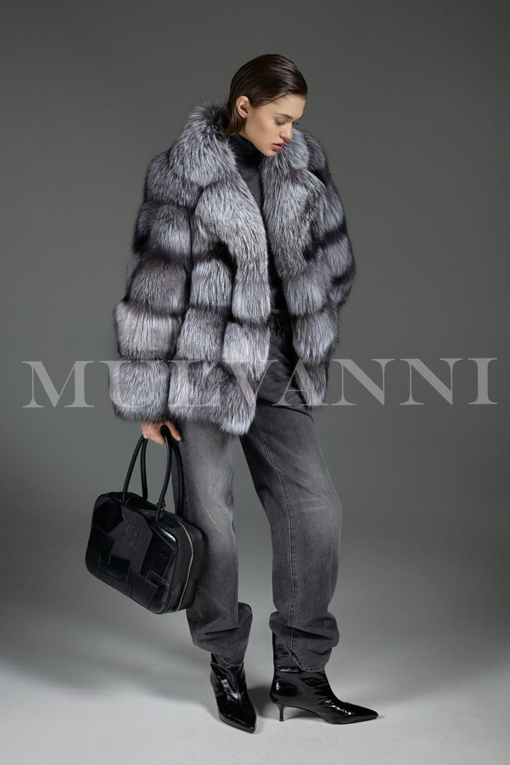 The soft, dense Silver Fox Fur drapes the woman stylishly, while a trendy black leather handbag completes the high-fashion cold-weather look.