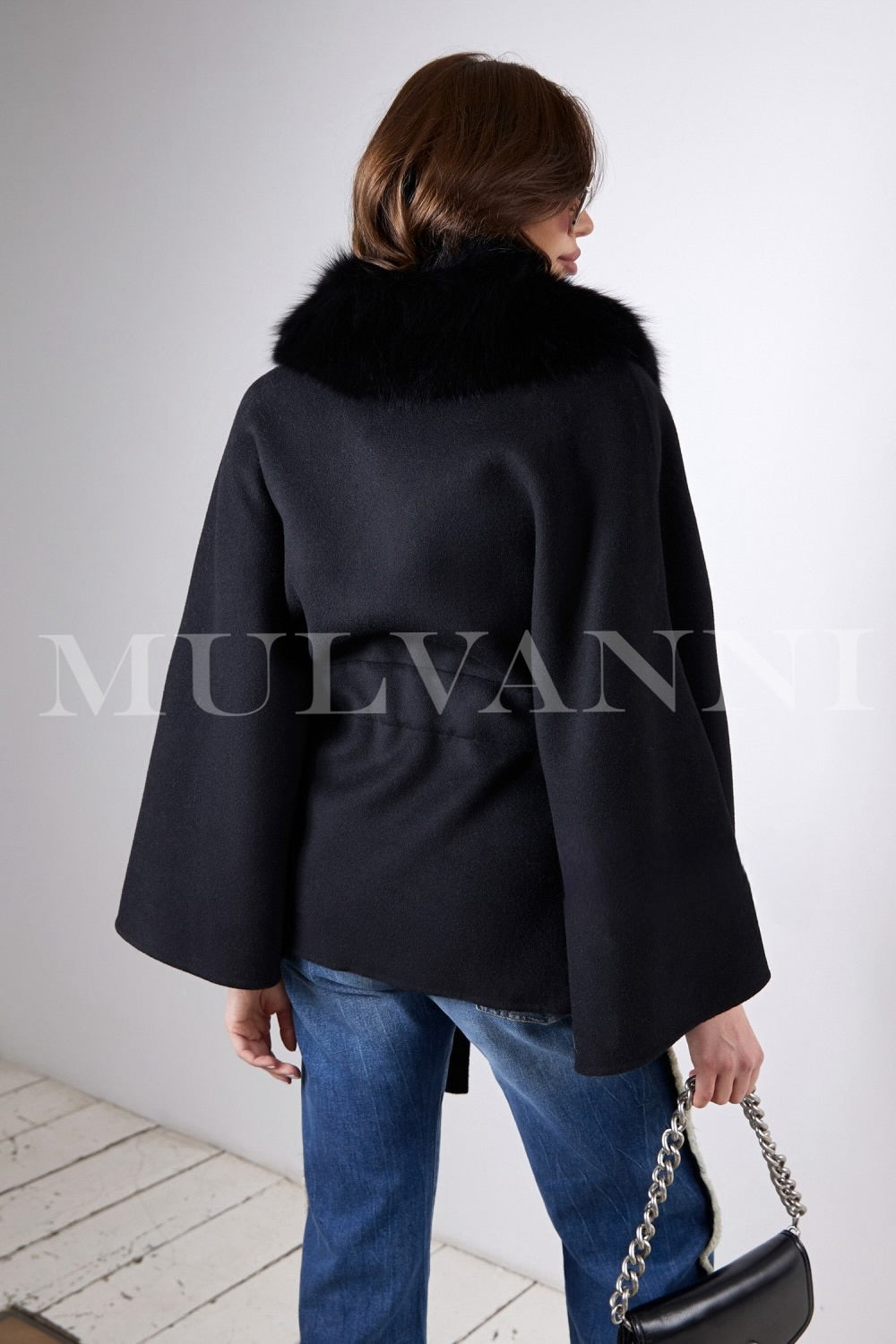 Wearing a sleek black cashmere cape with plush fox fur detailing, a woman exudes effortless glamour and versatility, ideal for layering over casual or formal attire.