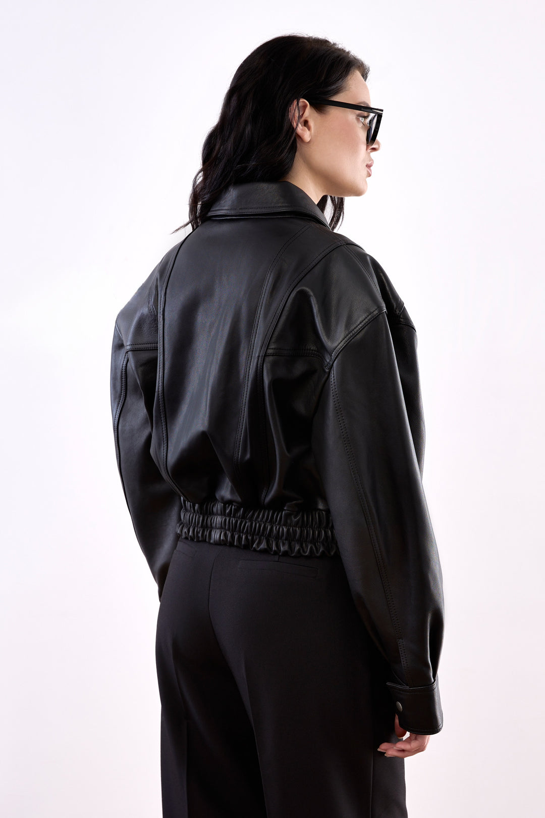 A woman models a chic cropped bomber jacket made from ultra-soft genuine leather, featuring a sophisticated finish and a contemporary fit just above the waist.