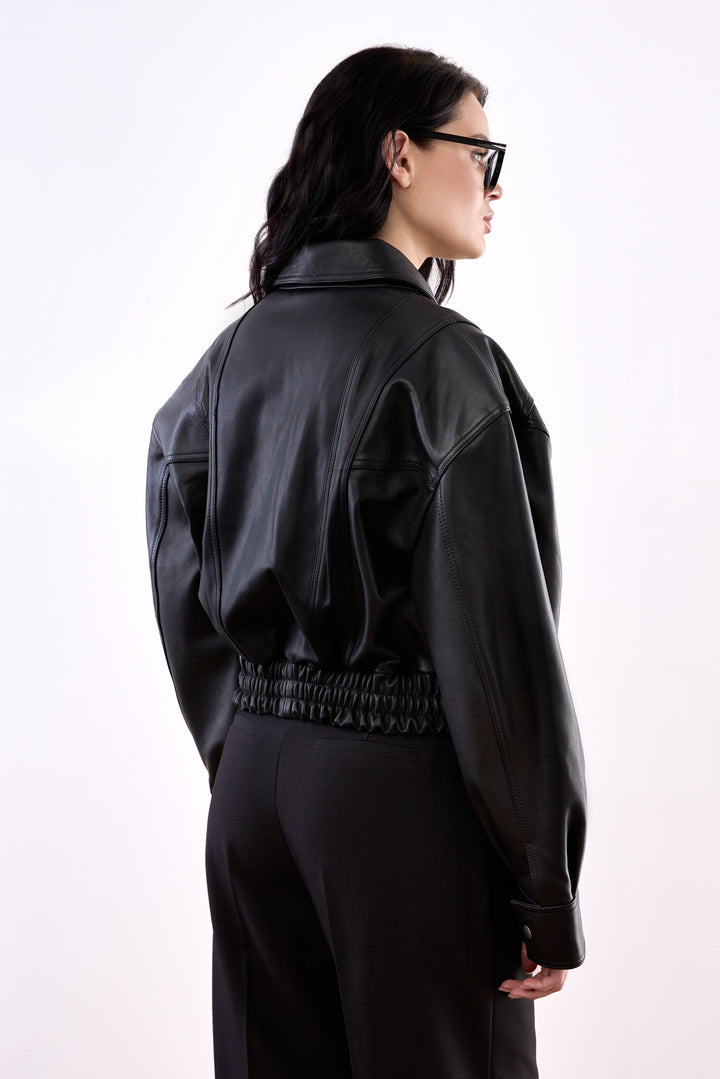 A woman models a chic cropped bomber jacket made from ultra-soft genuine leather, featuring a sophisticated finish and a contemporary fit just above the waist.