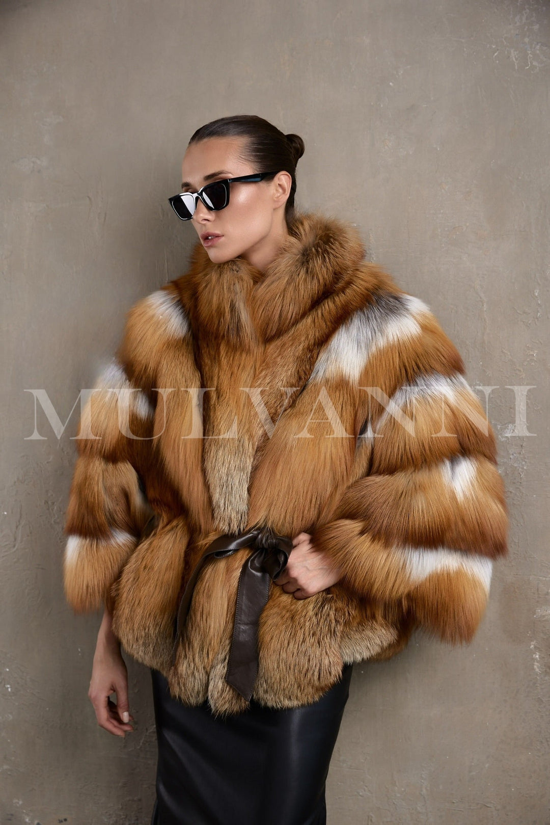 A woman showcases a striking red fox fur coat, featuring voluminous fur and an oversized cut that wraps her in warmth, while a leather belt adds tailored structure and timeless sophistication.