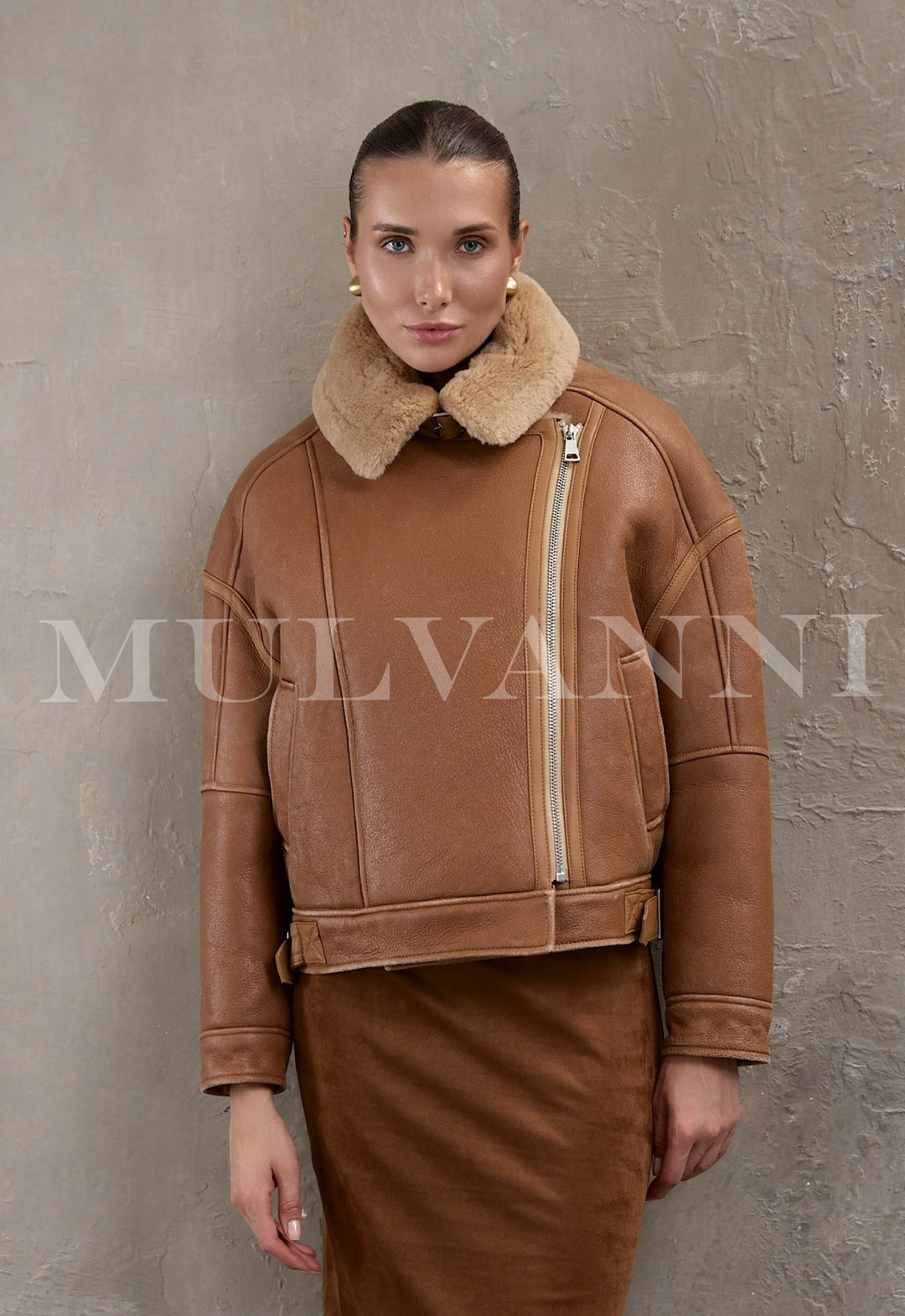 A woman wears a cropped brown aviator bomber crafted from thick sheepskin with plush shearling lining, styled in a modern oversized fit.