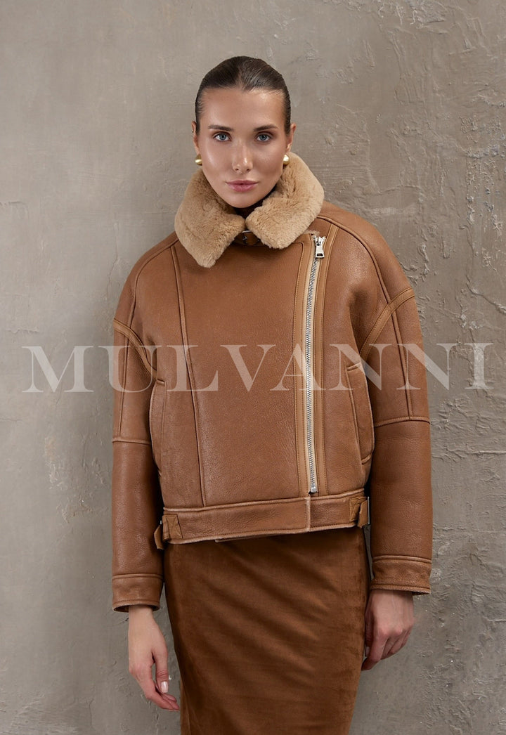 A woman wears a cropped brown aviator bomber crafted from thick sheepskin with plush shearling lining, styled in a modern oversized fit.