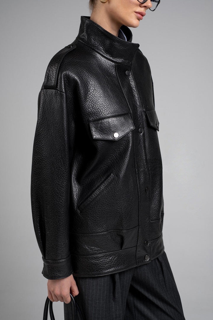 A woman wearing a modern black genuine leather jacket with a sleek high collar and tailored fit, paired with fashionable glasses and a black leather bag for effortless winter style.