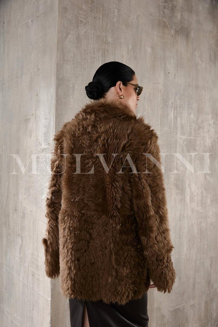 A stylish woman in a premium brown shearling coat, embodying both cozy comfort and elegant fashion with its thick, soft fabric and classic appeal.