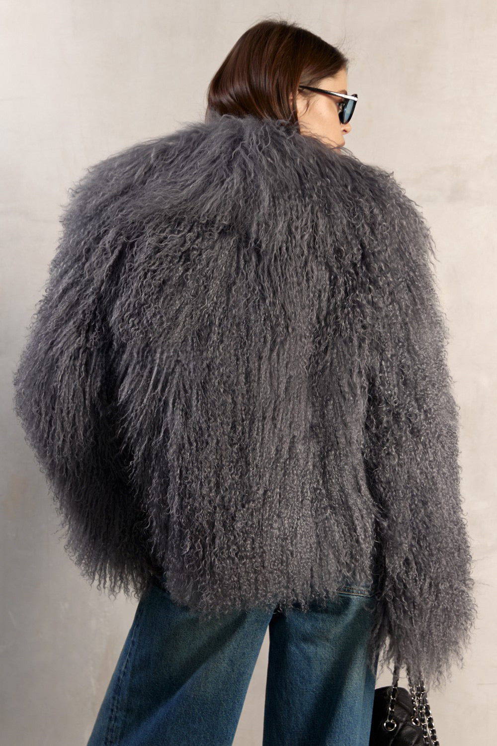 A woman dressed in a handcrafted grey Mongolian fur coat, showcasing long sleeves, a dramatic collar, and a refined silhouette with satin and leather lining for a sophisticated look.