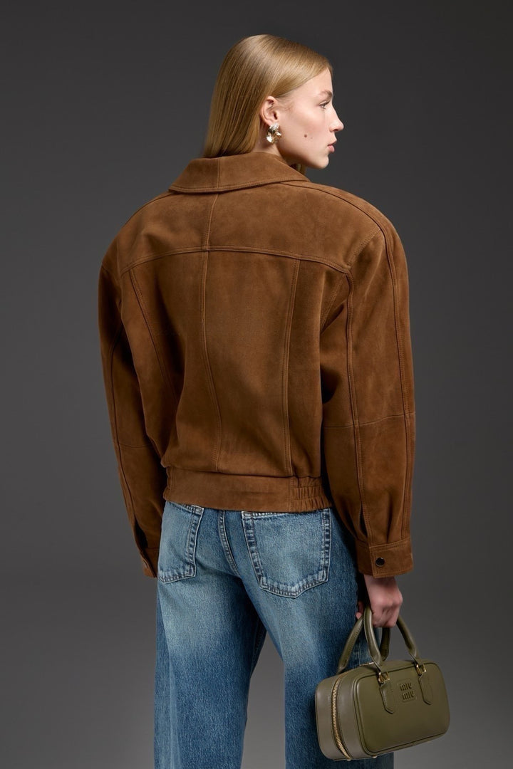 Draped in a brown suede jacket, a woman showcases a modern, structured design with a cropped cut perfect for a chic wardrobe.