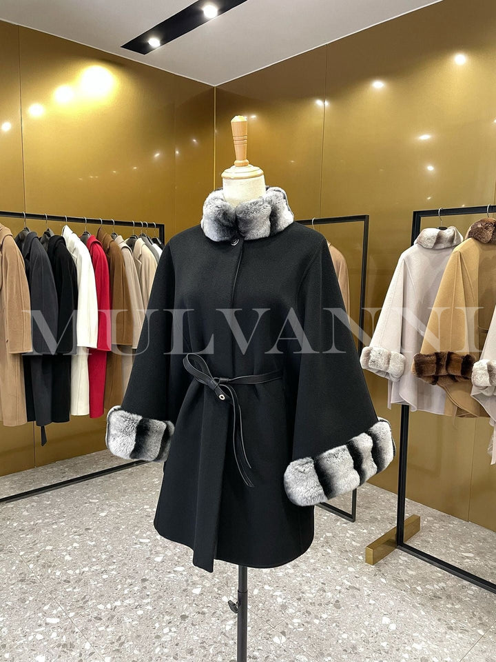 Women’s black cashmere cape with gray rex rabbit fur trim, featuring a leather belt and structured funnel neckline, displayed in a boutique.