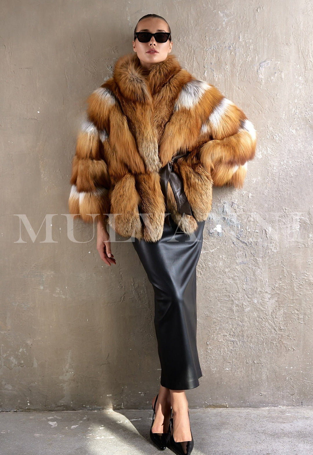 A woman wears a luxurious oversized coat made from genuine red fox fur, cinched at the waist with a sleek leather belt, radiating elegance and warmth in a refined winter look.