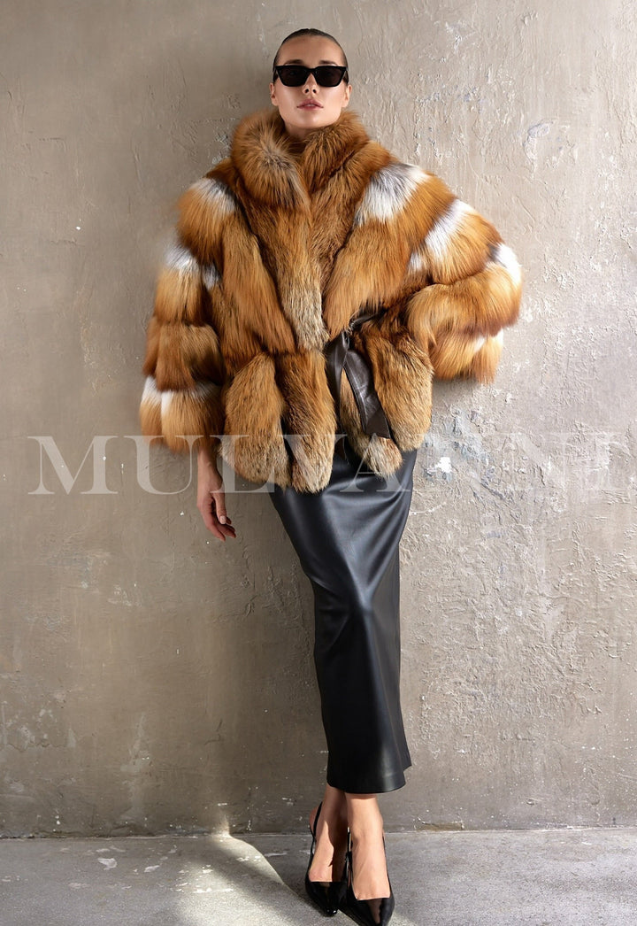 A woman wears a luxurious oversized coat made from genuine red fox fur, cinched at the waist with a sleek leather belt, radiating elegance and warmth in a refined winter look.